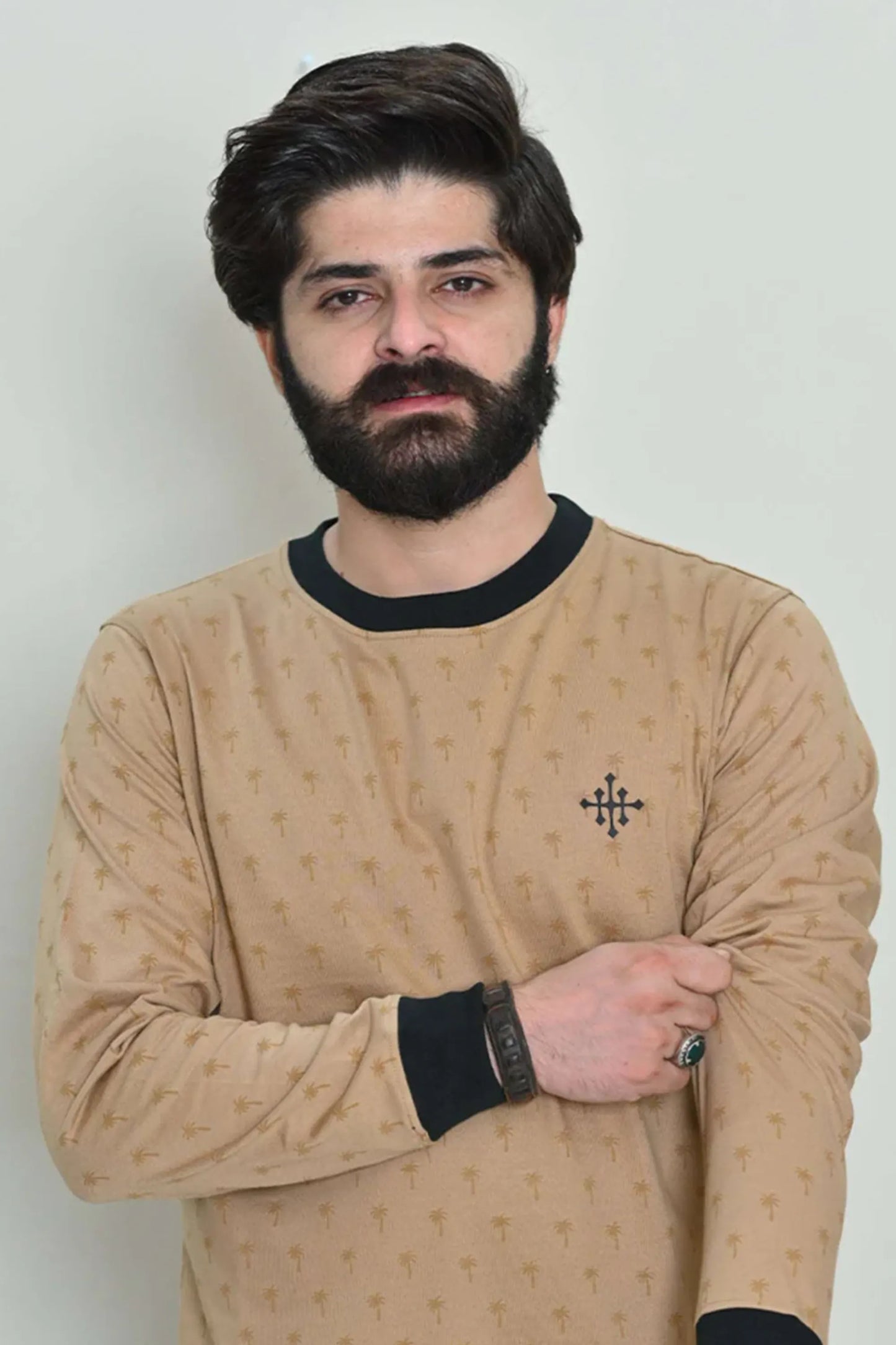Casual crossed-arm pose wearing a beige sweatshirt with palm motifs