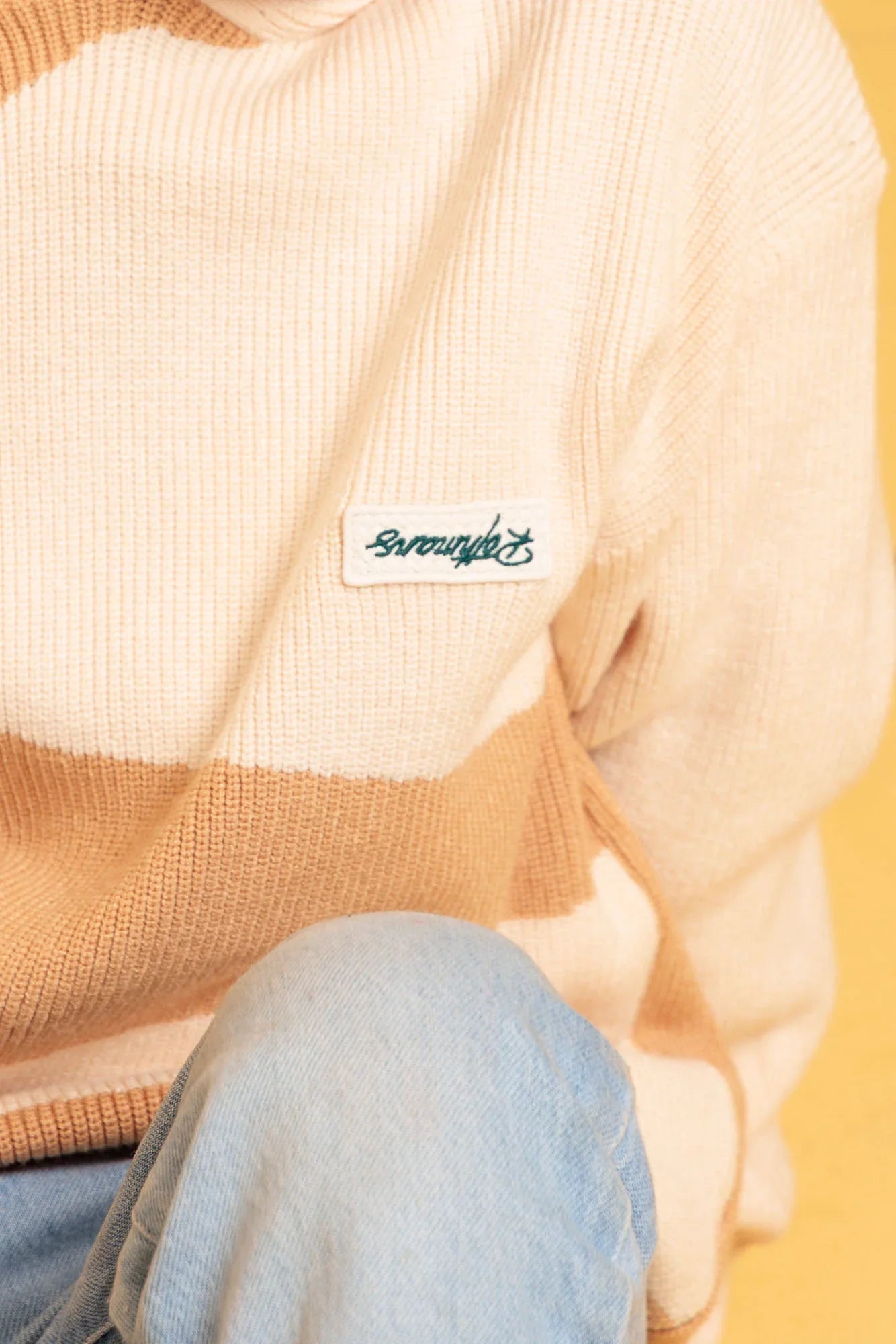 Beige sweater with a brand label on a yellow background