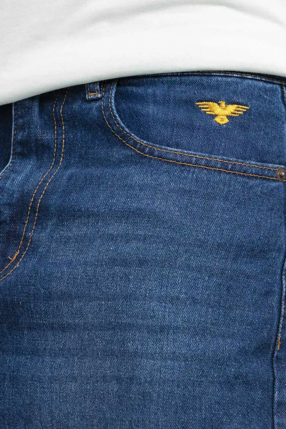 Close-up of blue jeans with a gold eagle logo on the pocket.