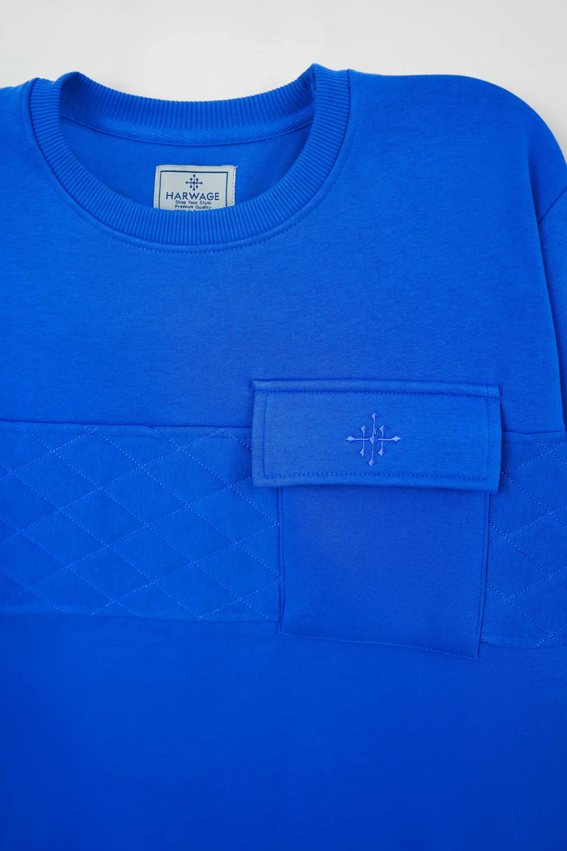 Blue sweatshirt with a pocket and visible brand label on a light gray background