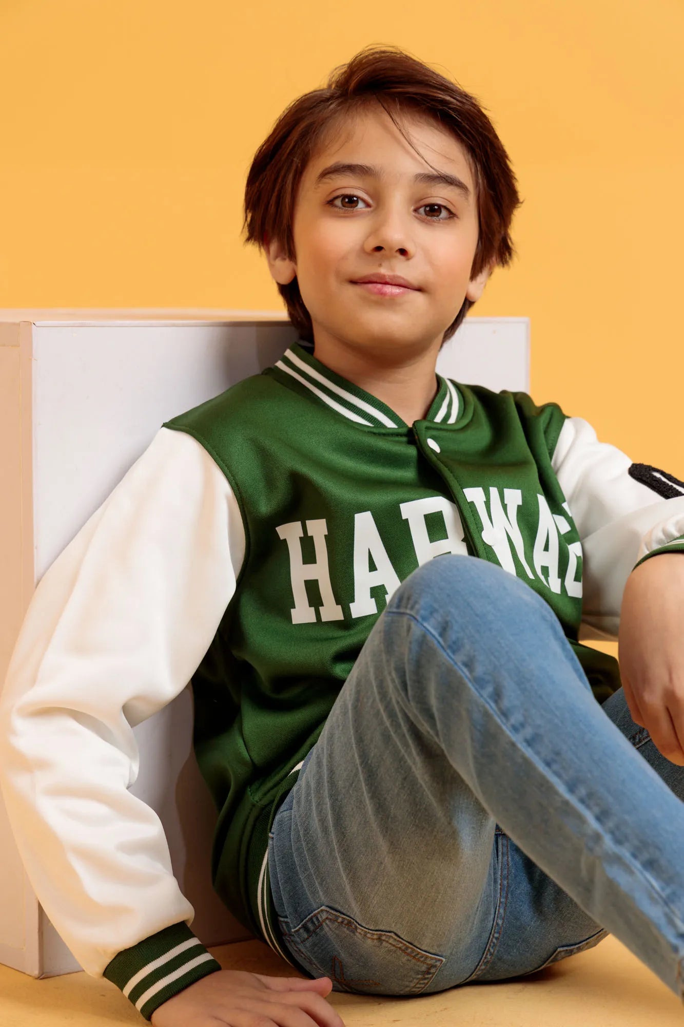 Junior boy sitting casually in a green varsity jacket and jeans