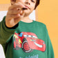 Child wearing a green sweatshirt with a Lightning McQueen design on a yellow background