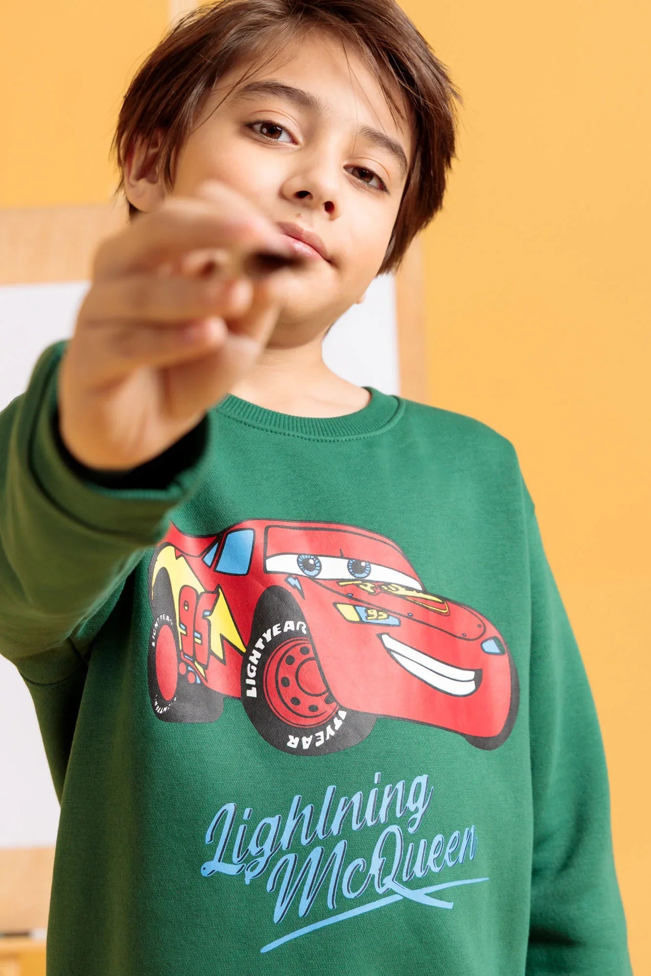 Child wearing a green sweatshirt with a Lightning McQueen design on a yellow background