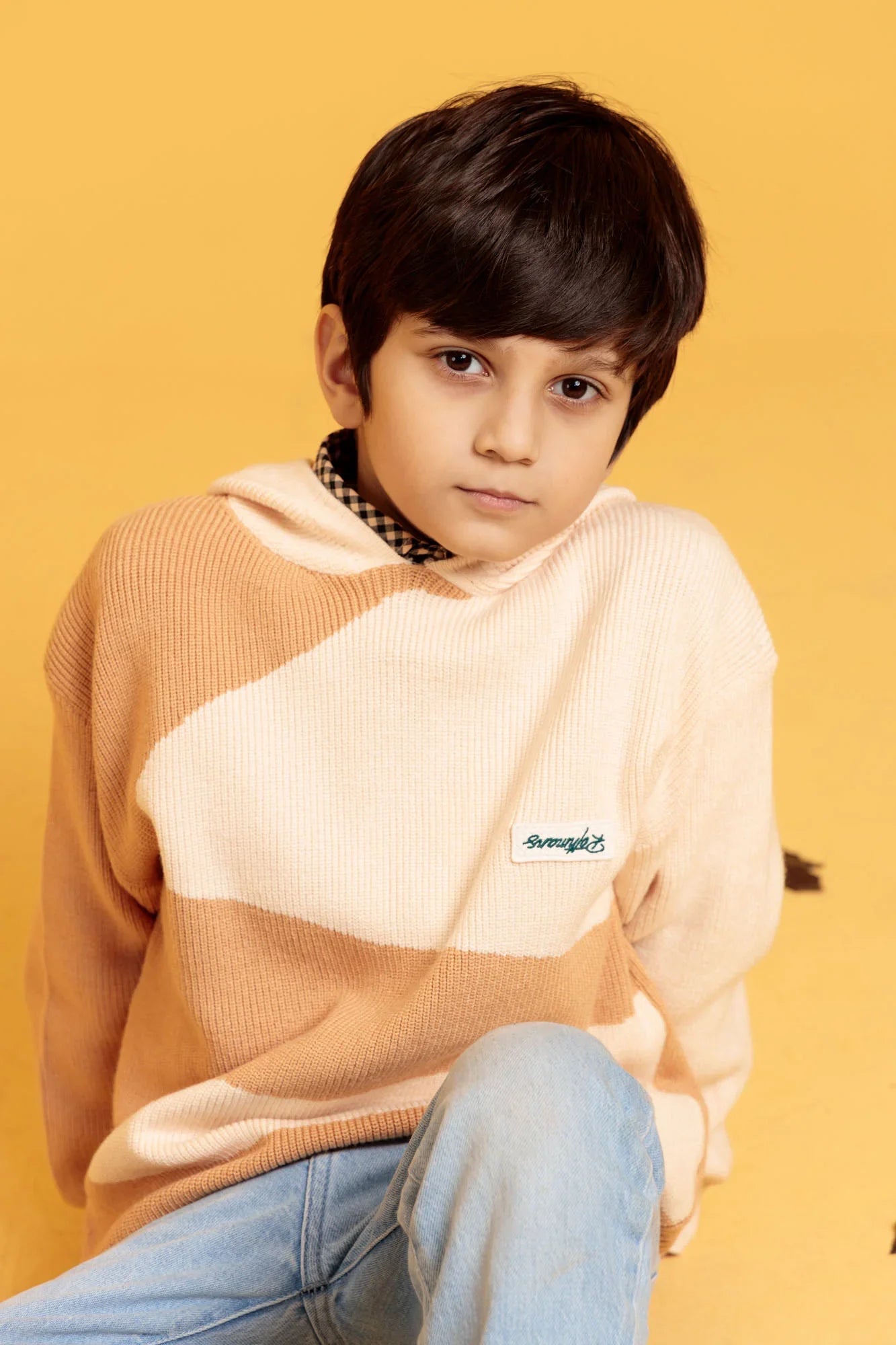 Child wearing a striped sweater with a brand logo on a yellow background