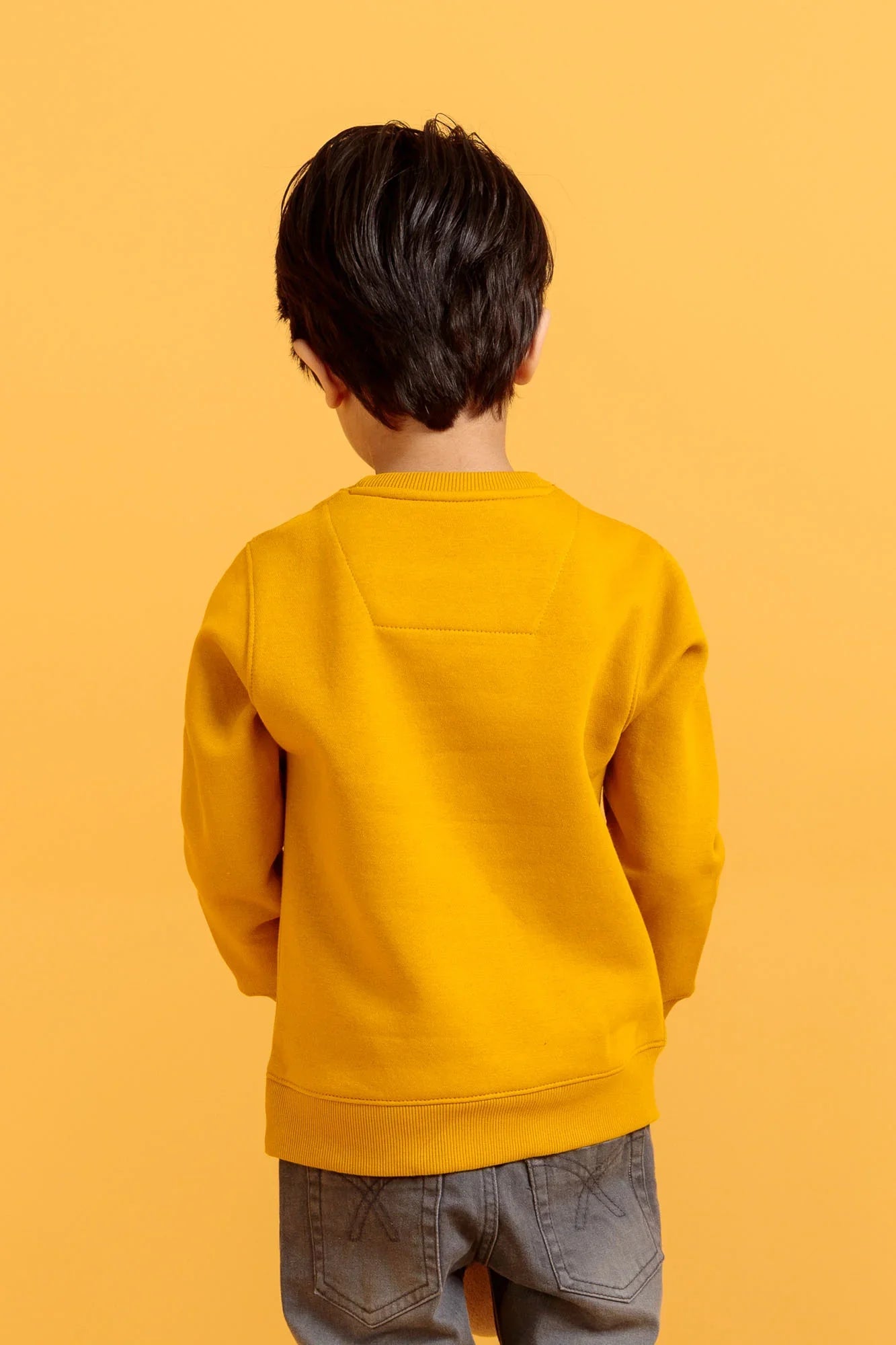 Child wearing a yellow sweatshirt against an orange background