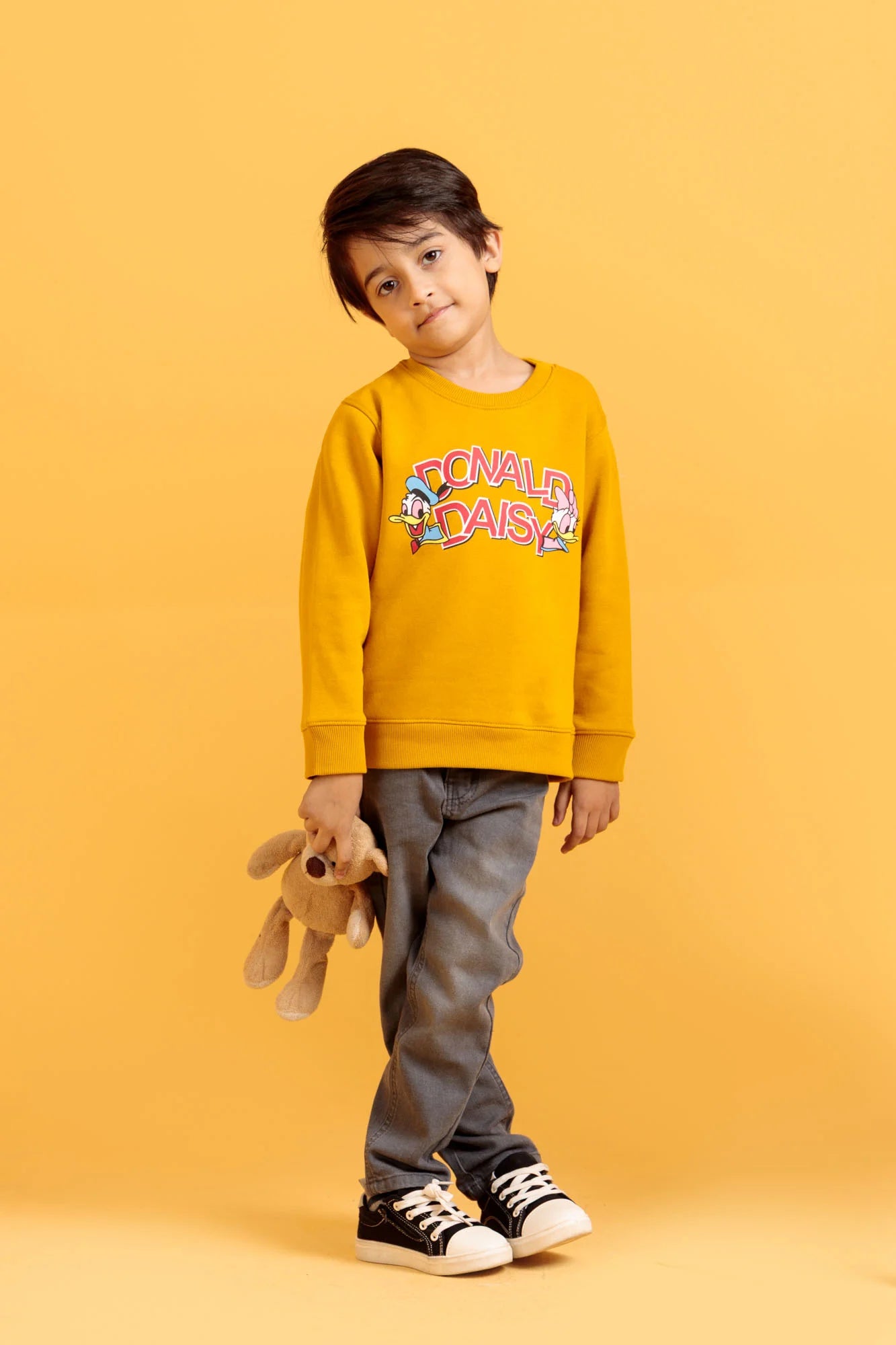 Child wearing a yellow sweatshirt with cartoon characters on an orange background