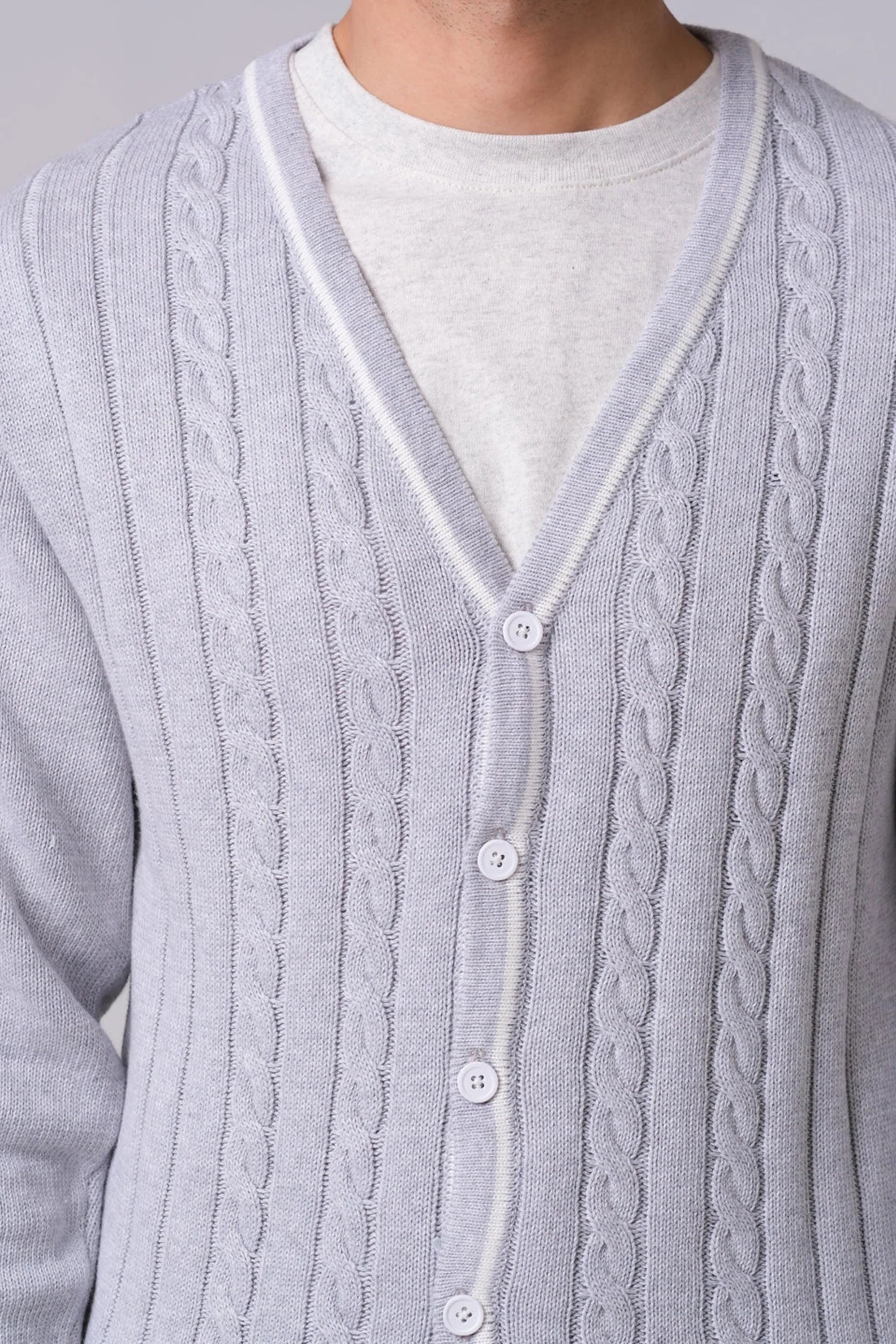 Close-up of a cable knit cardigan with buttons on a plain background