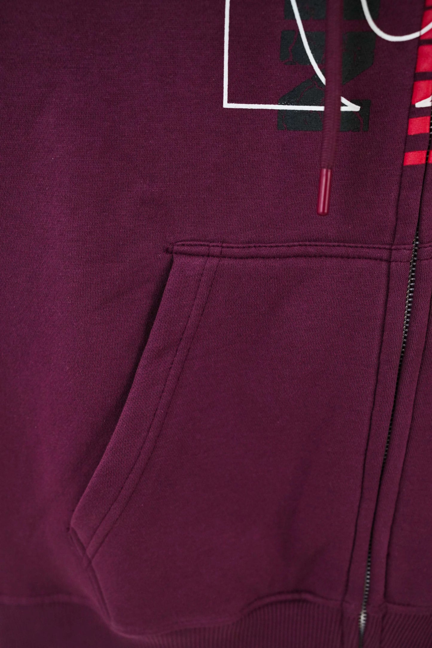 Close-up of a maroon hoodie with a zipper and logo on a dark background