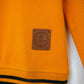 Close-up of an orange sweater with a brand label on a white background