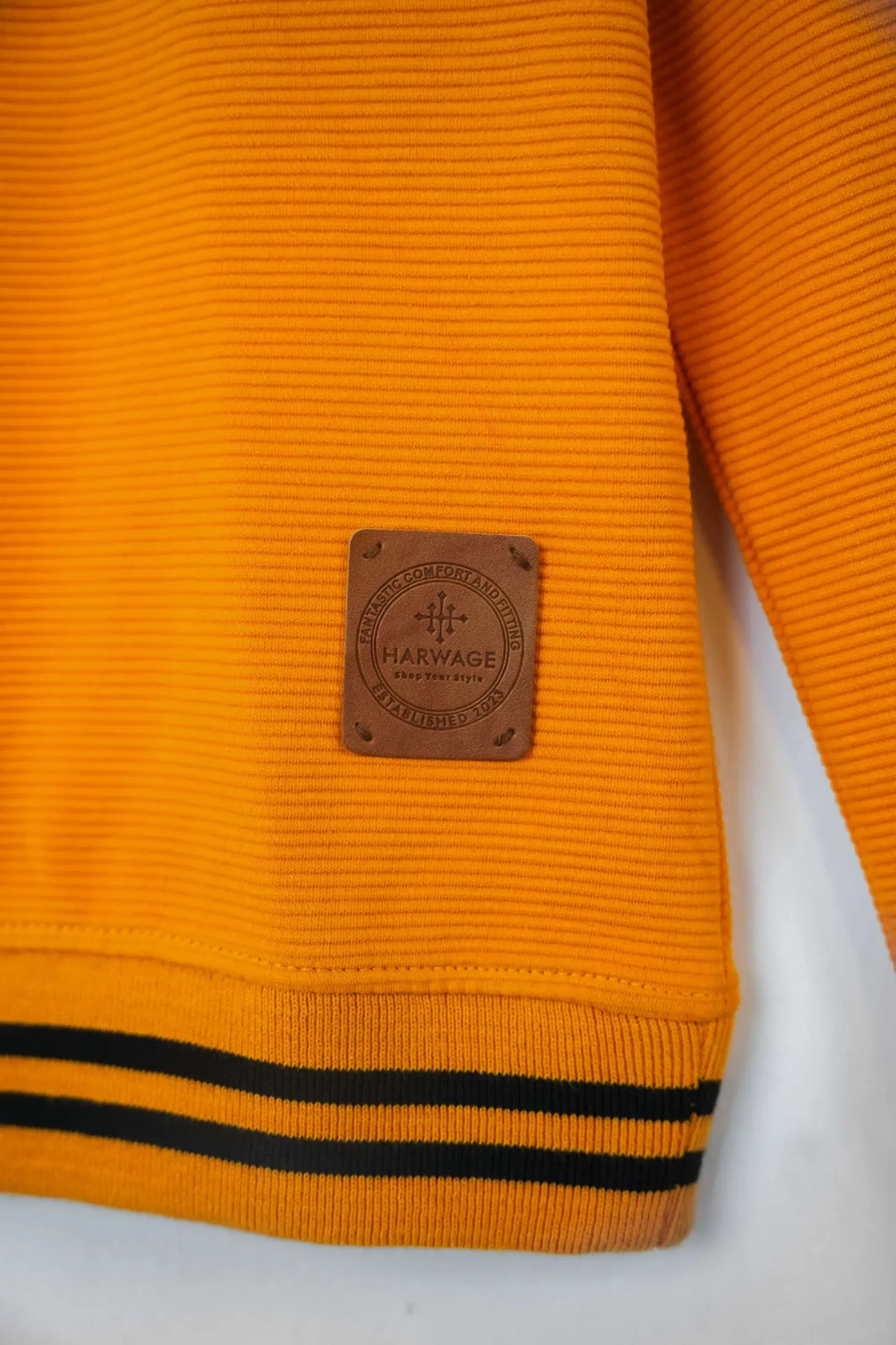Close-up of an orange sweater with a brand label on a white background