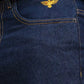 Close-up of a blue denim pants with an embroidered gold eagle logo.