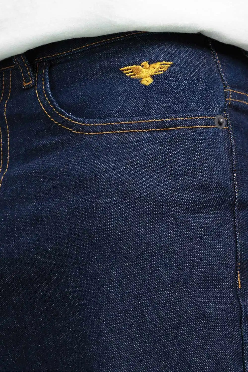 Close-up of a blue denim pants with an embroidered gold eagle logo.
