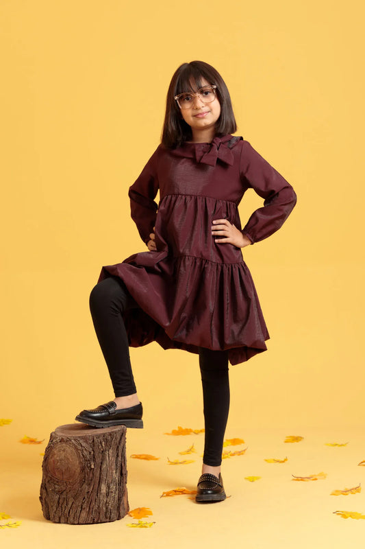 Girl in a burgundy dress standing on a wooden stump with a yellow background