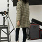 Girl in a checkered coat standing in a photography studio with equipment.