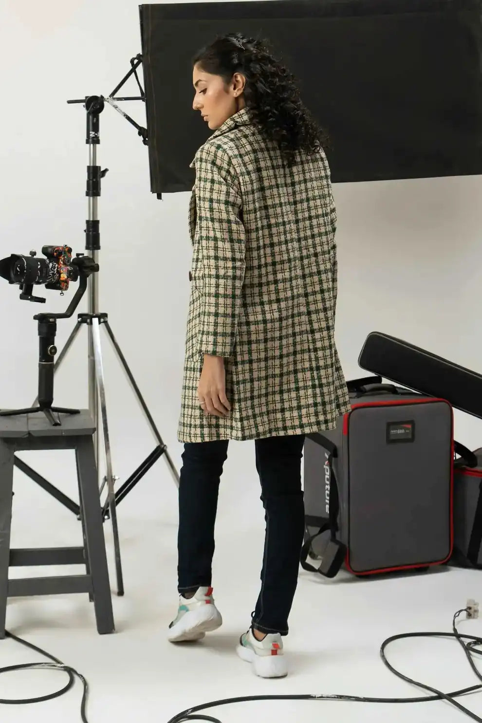 Girl in a checkered coat standing in a photography studio with equipment.