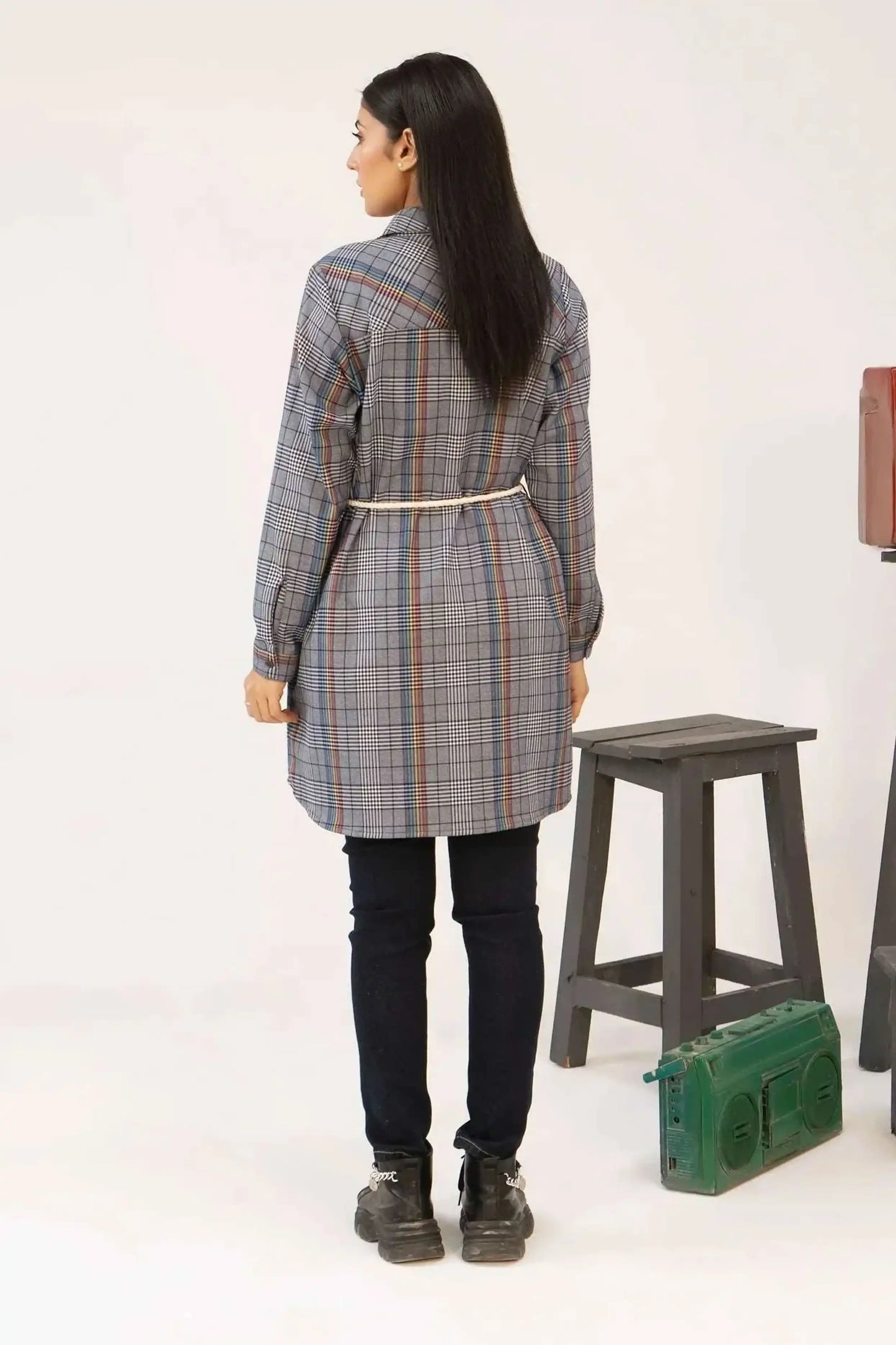 Girl wearing a plaid coat standing next to a stool and a green radio