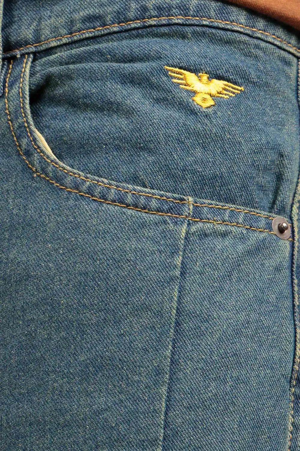 Close-up of blue denim jeans with a gold eagle logo on the pocket
