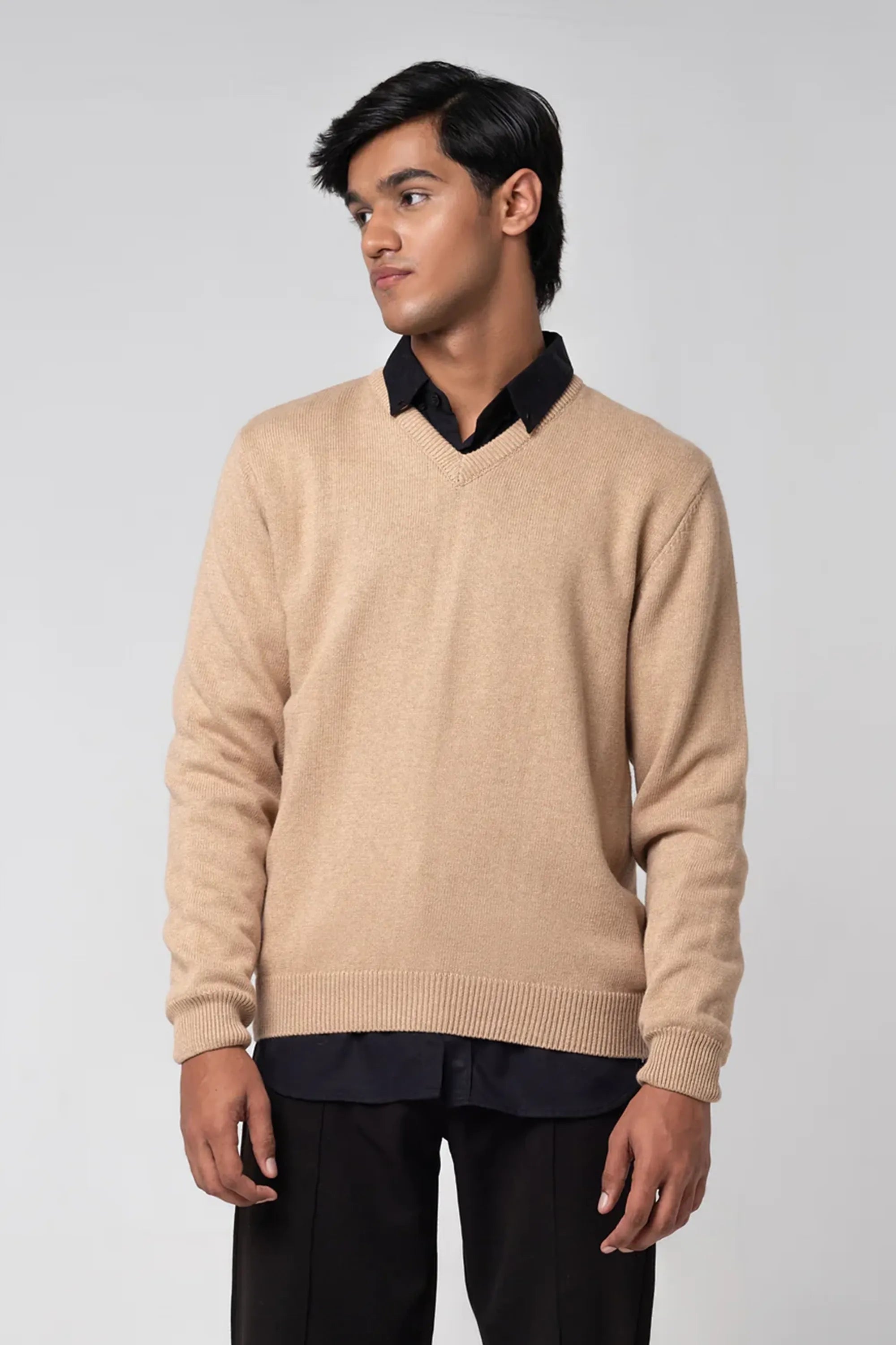 Man wearing a beige sweater over a black shirt on a white background