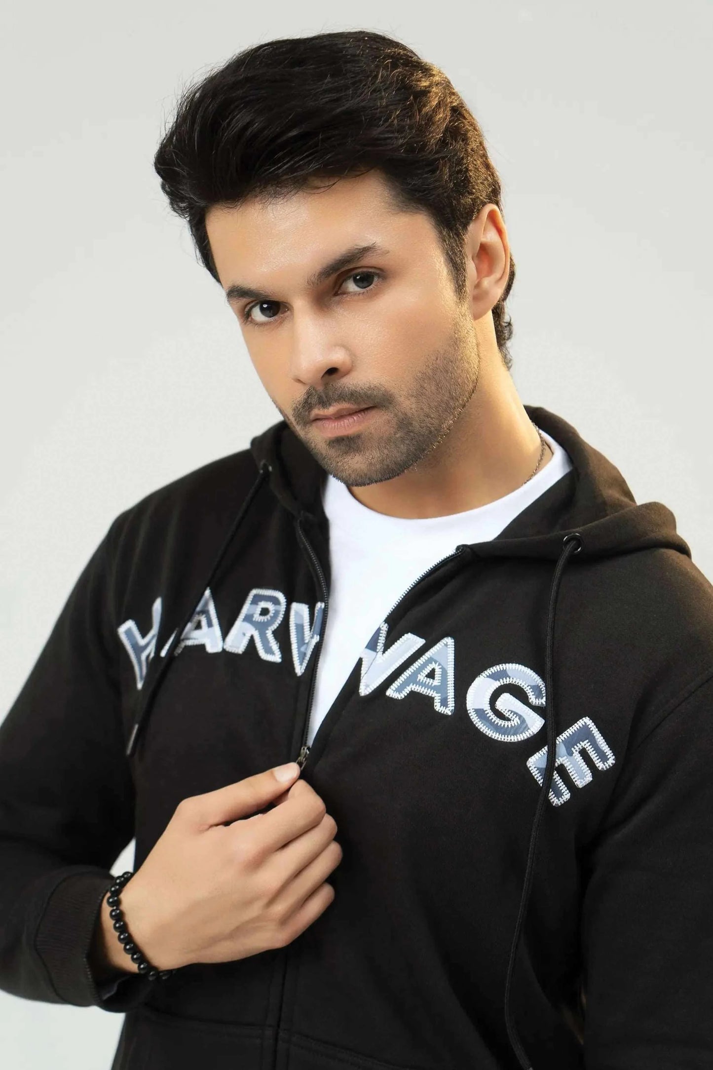 Man wearing a black hoodie with 'Harvard' printed on it against a plain background