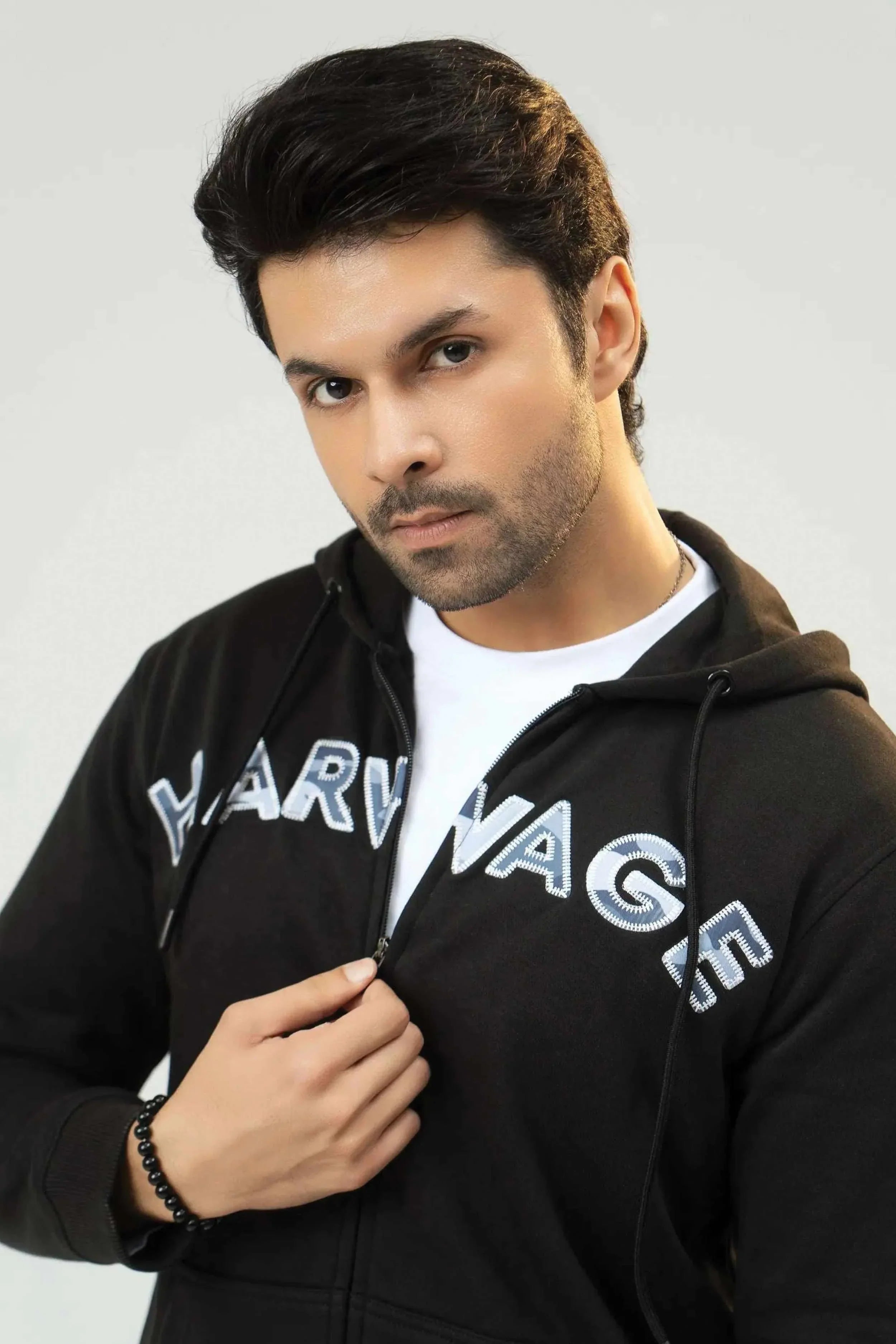 Man wearing a black hoodie with 'Harvard' printed on it against a plain background