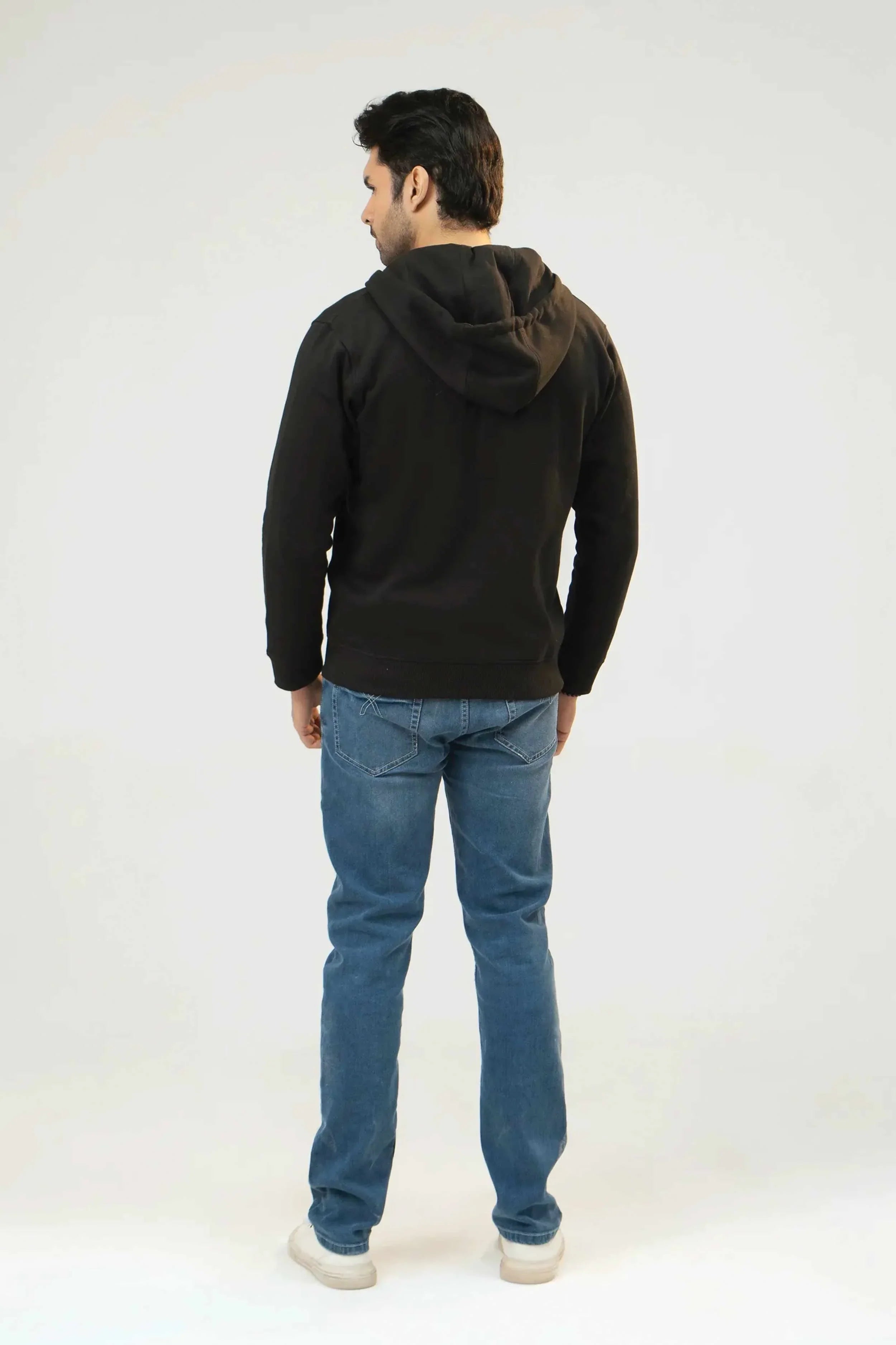 Man wearing a black hoodie and blue jeans on a white background