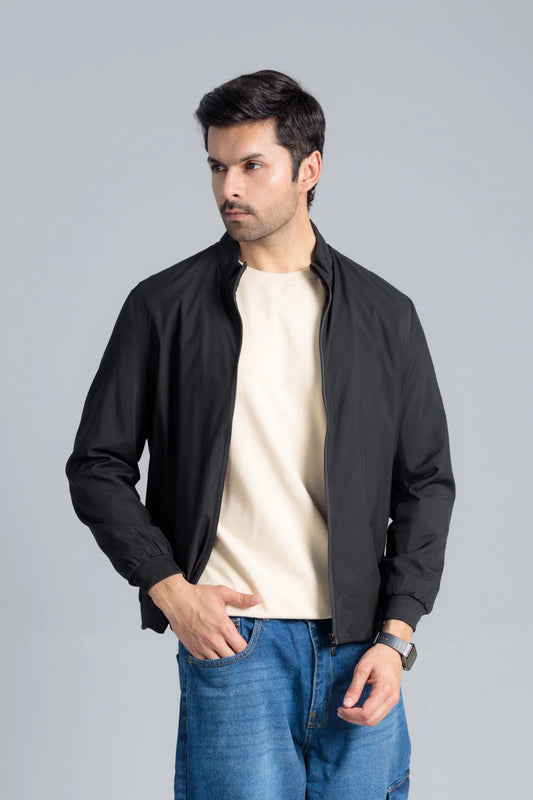 Man wearing a black jacket over a white shirt and blue jeans on a gray background