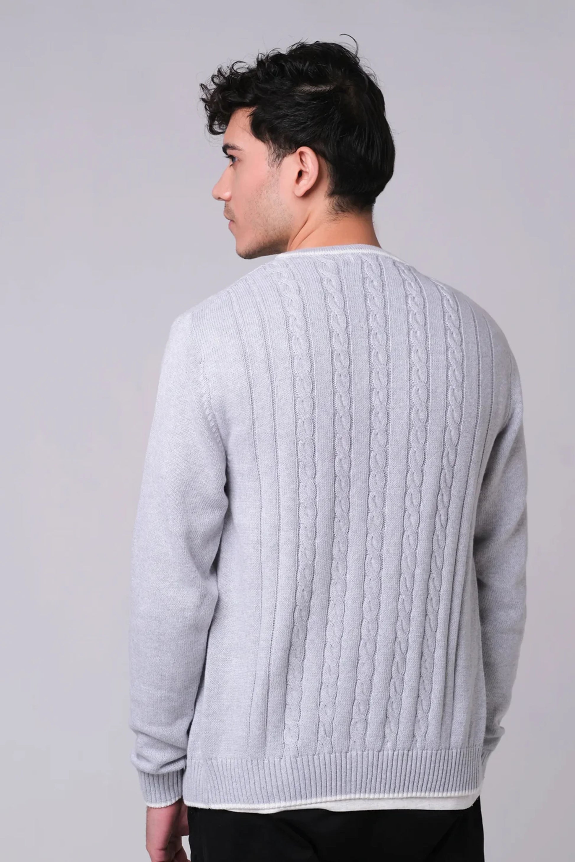 Man wearing a gray cable knit sweater against a plain background