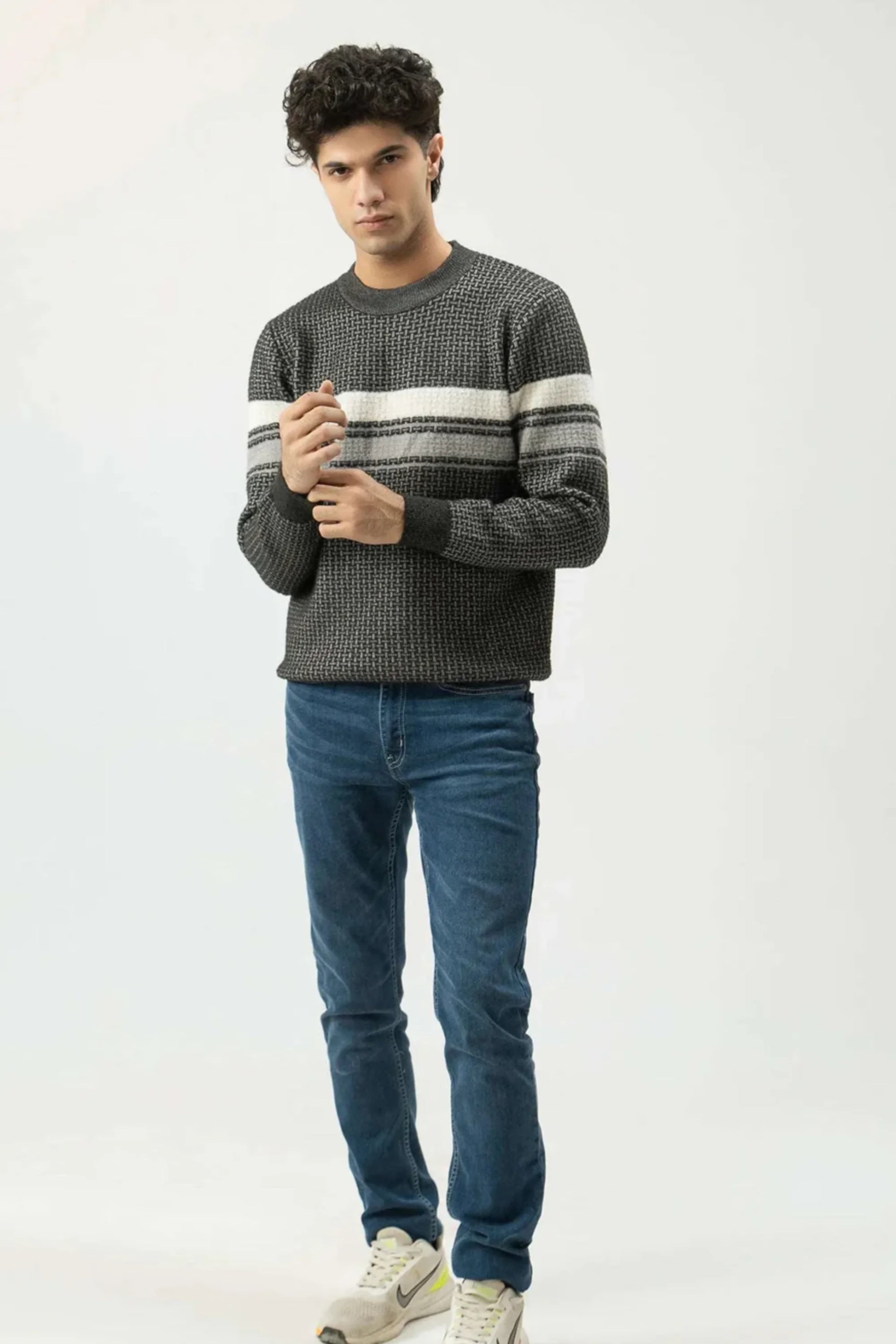 Man wearing a gray sweater with white stripes and blue jeans on a white background