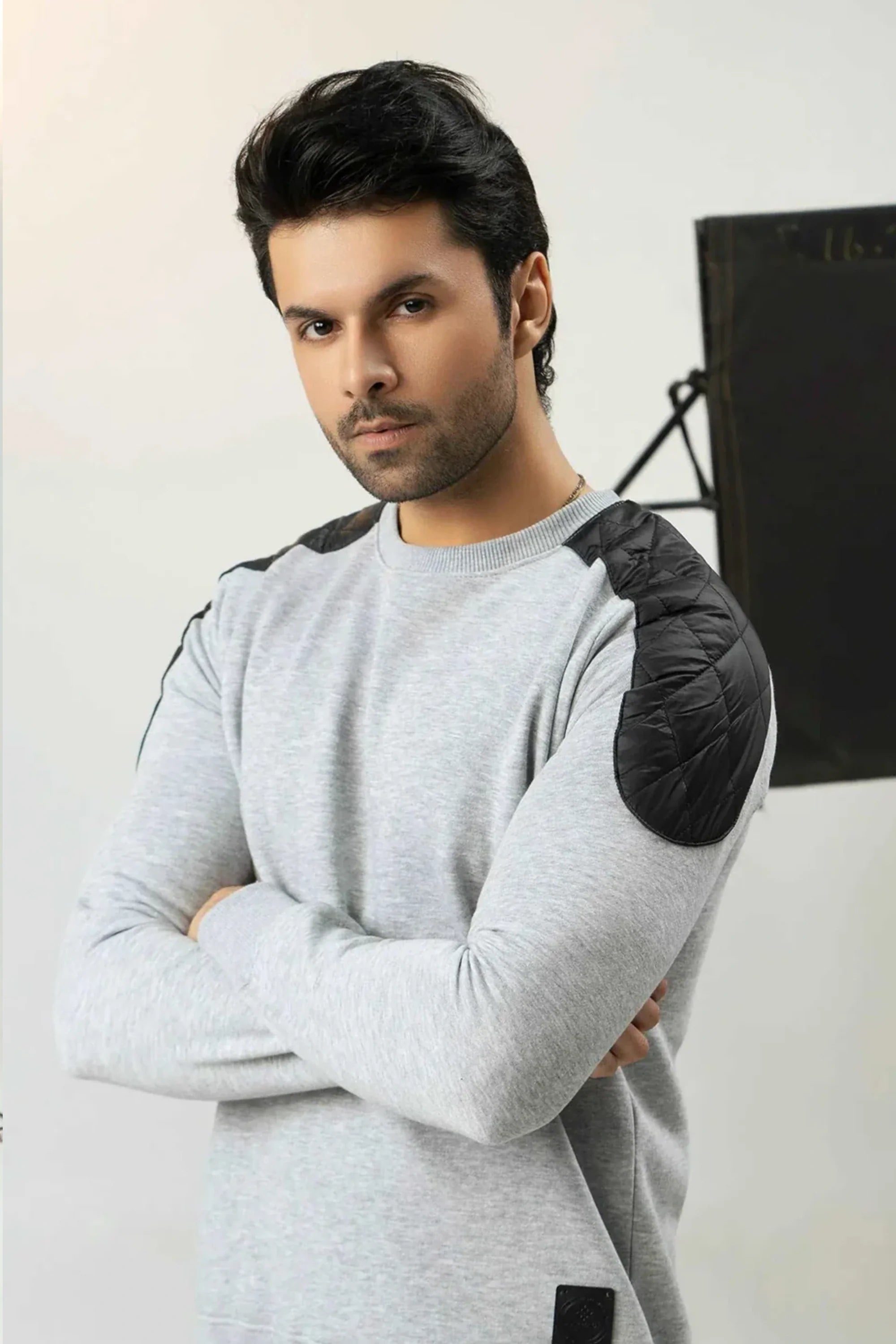 Man wearing a gray sweater with black shoulder pads against a white background