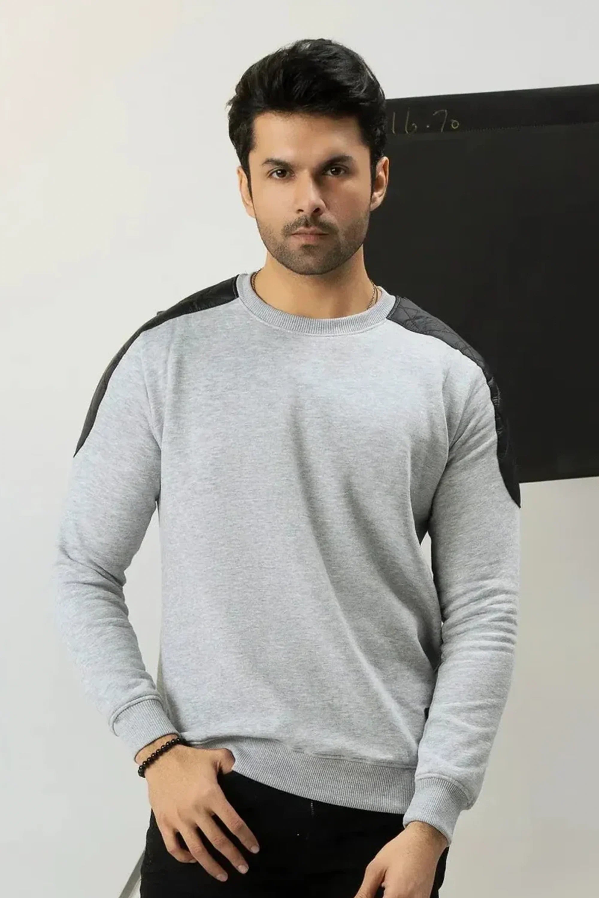 A man wearing a gray sweater with black sleeves against a plain background