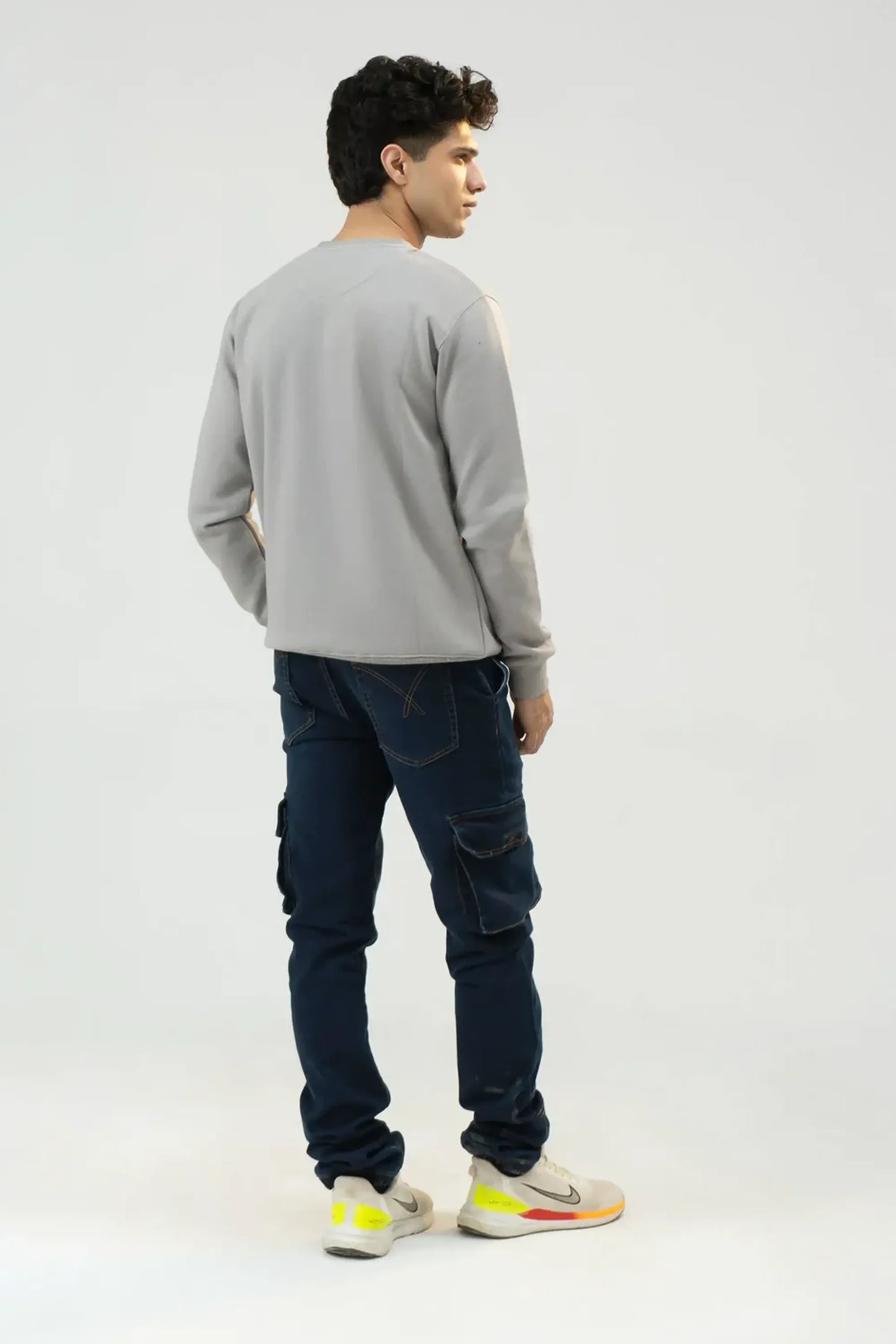 Man wearing a gray sweatshirt and dark blue jeans on a white background
