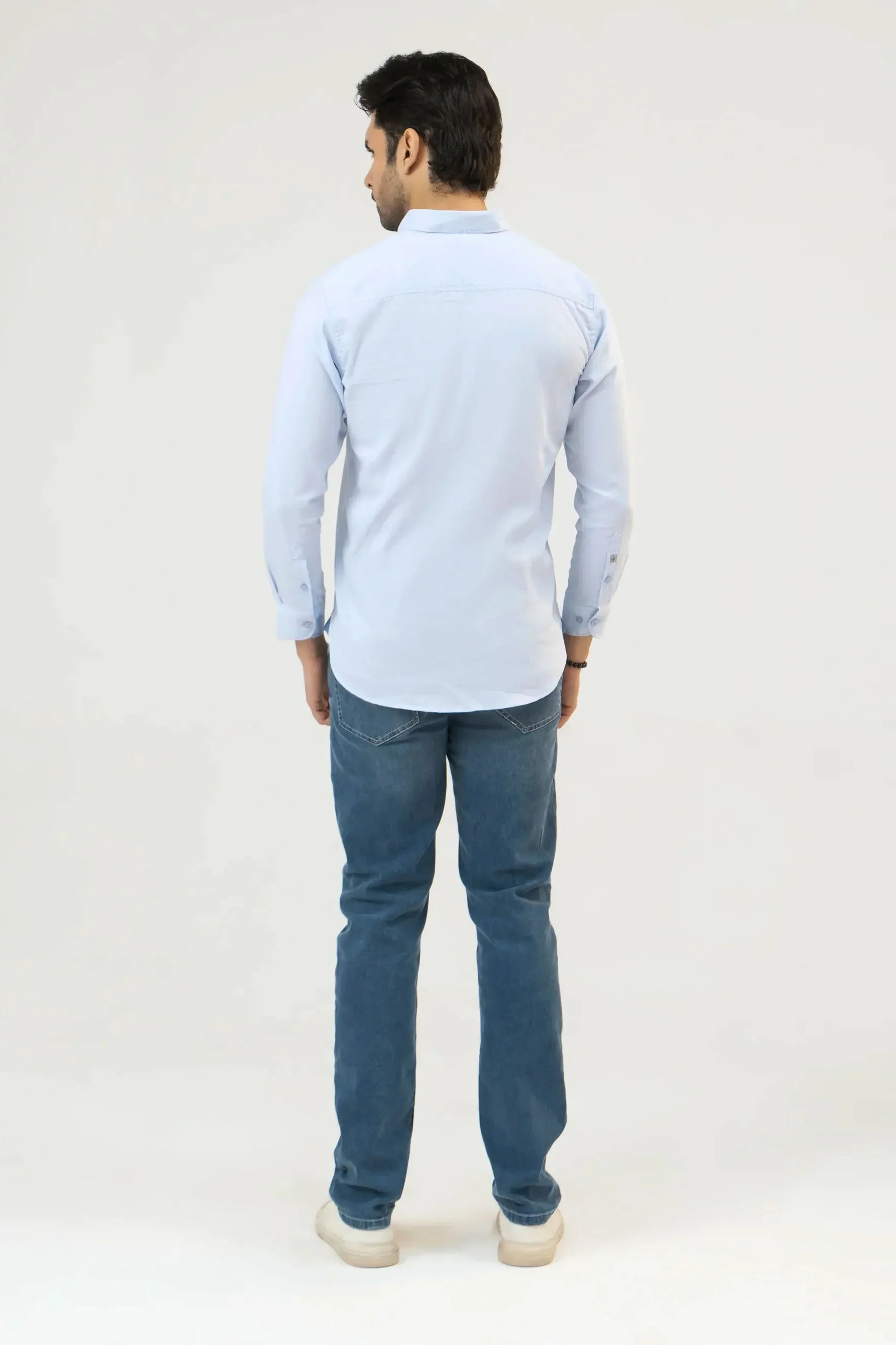 Man wearing a light blue shirt and denim jeans on a white background