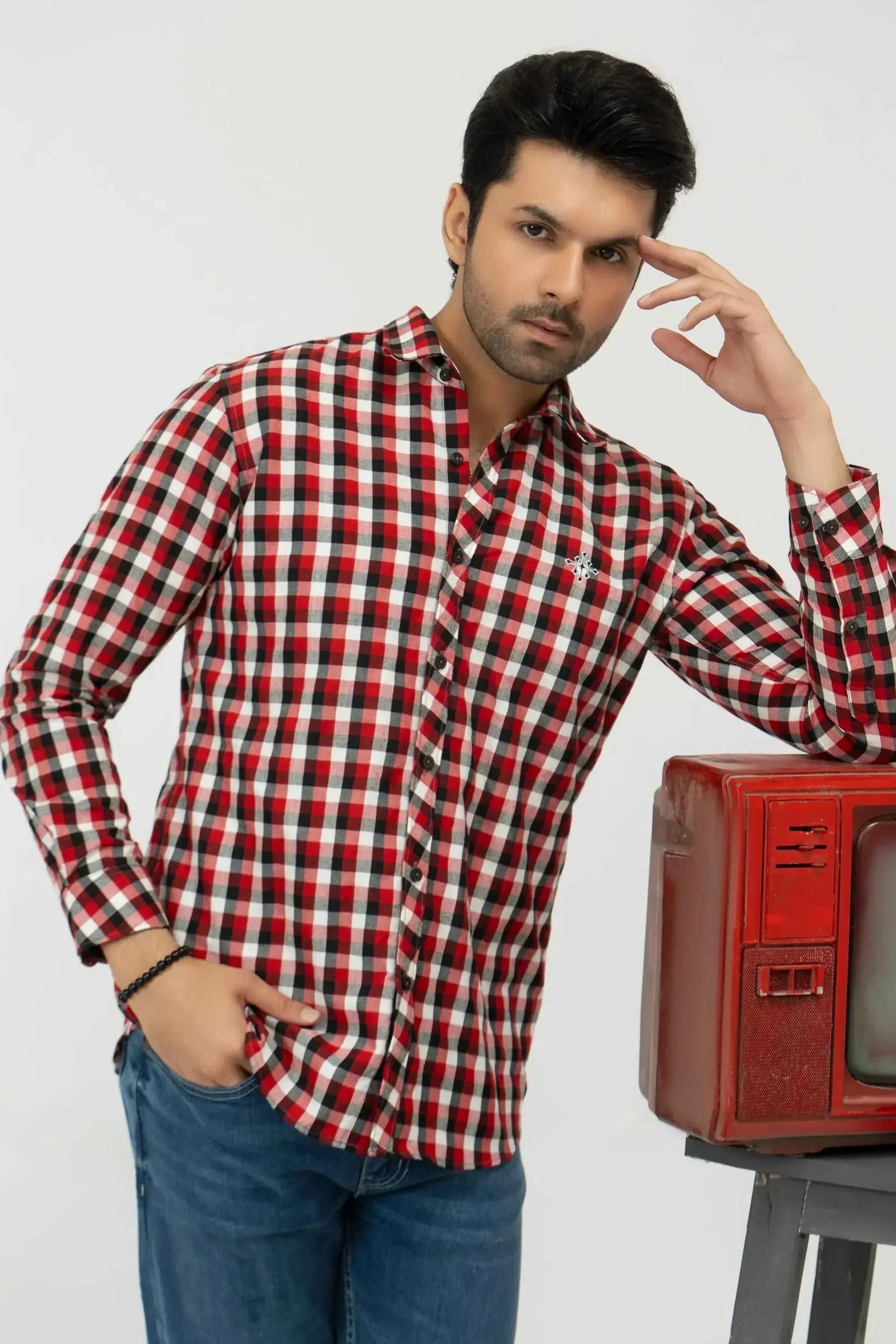 Man wearing a red and white checkered shirt with a vintage red television set 
