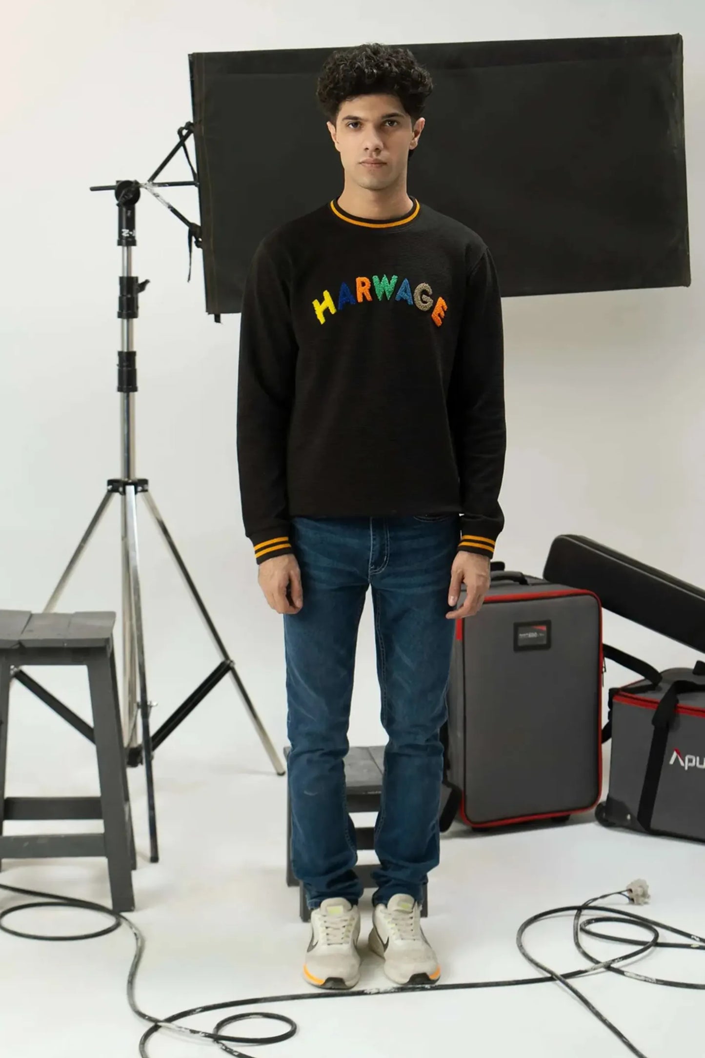Person wearing a black sweatshirt with colorful text, standing in a studio setting