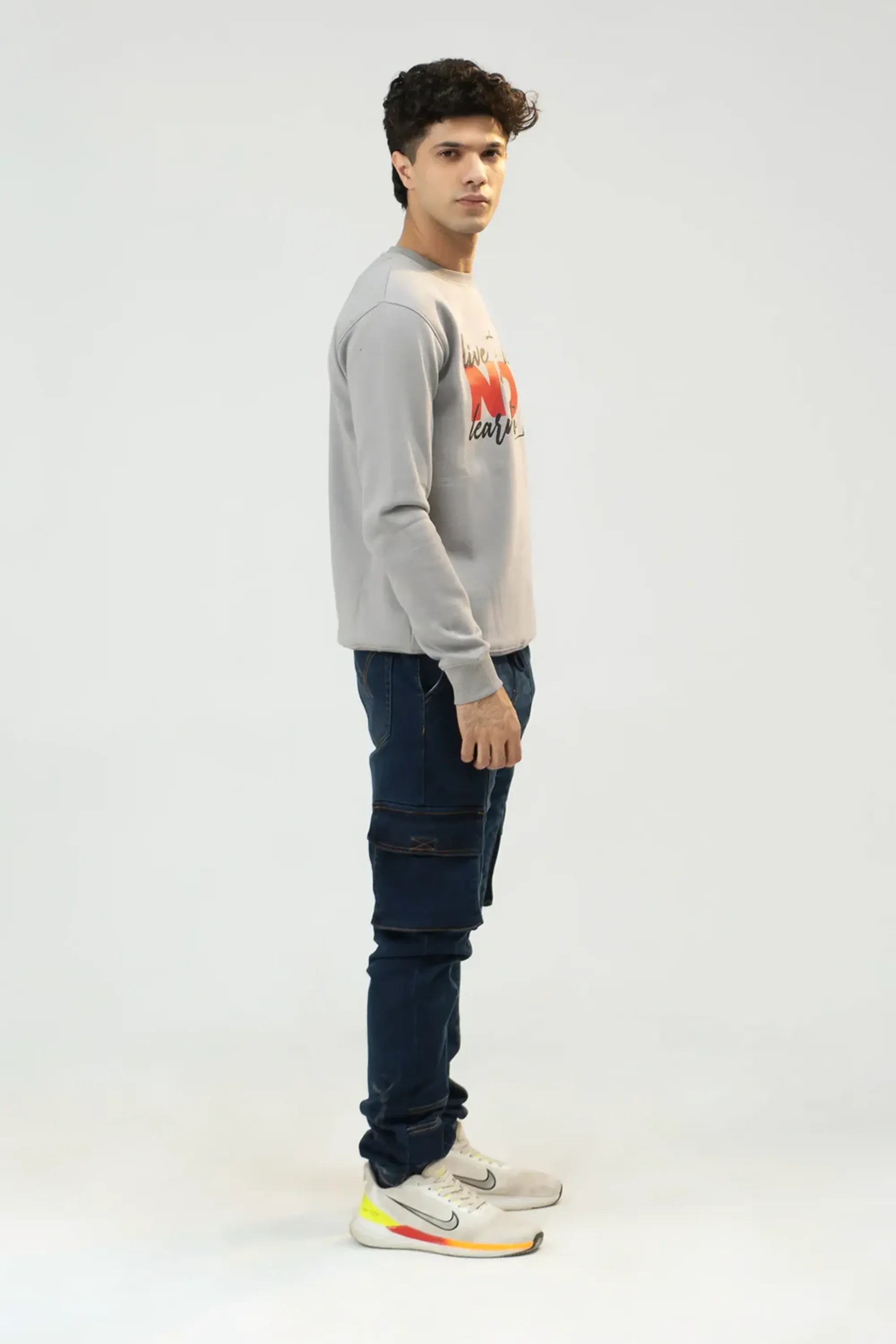 Person wearing a gray sweater with a colorful design and dark jeans on a white background
