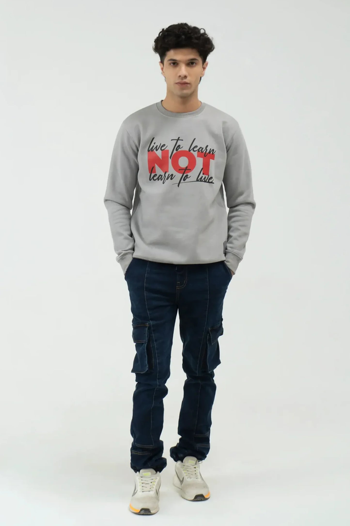 Person wearing a gray sweatshirt with text and dark jeans on a white background