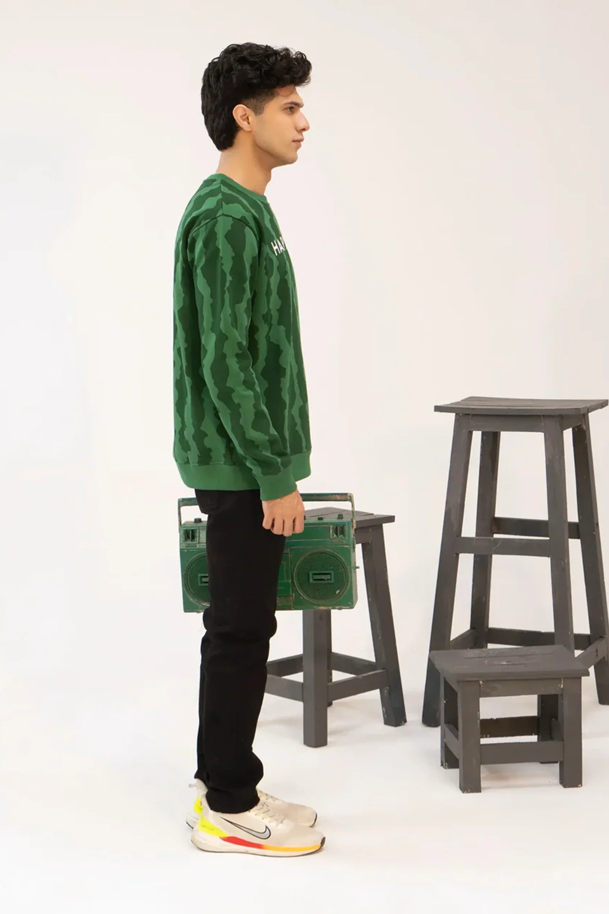 Person wearing a green patterned sweater standing next to stools on a white background