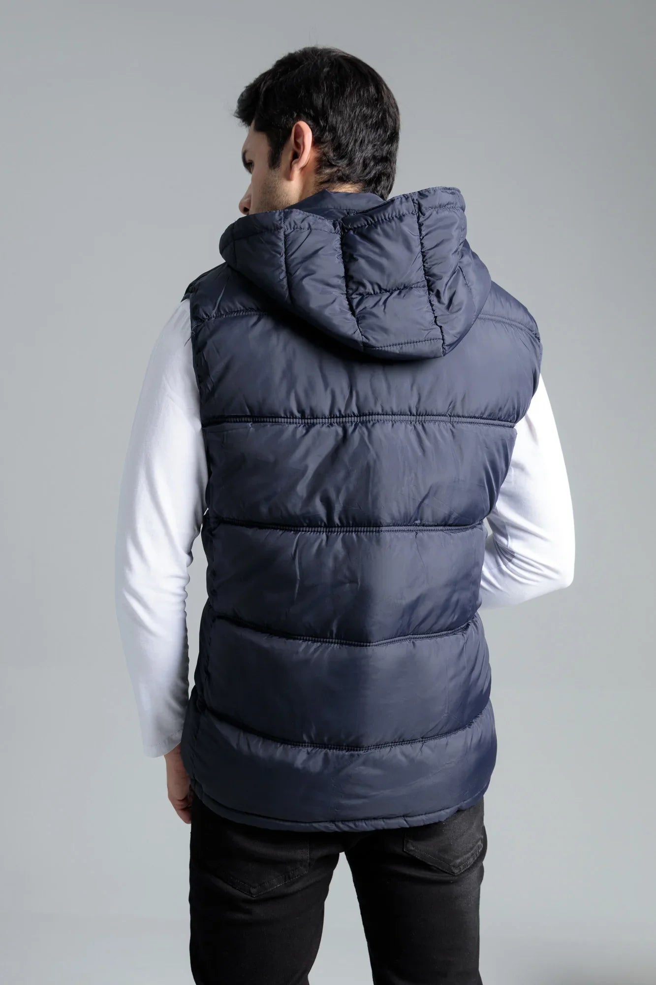 Person wearing a navy puffer vest on a gray background