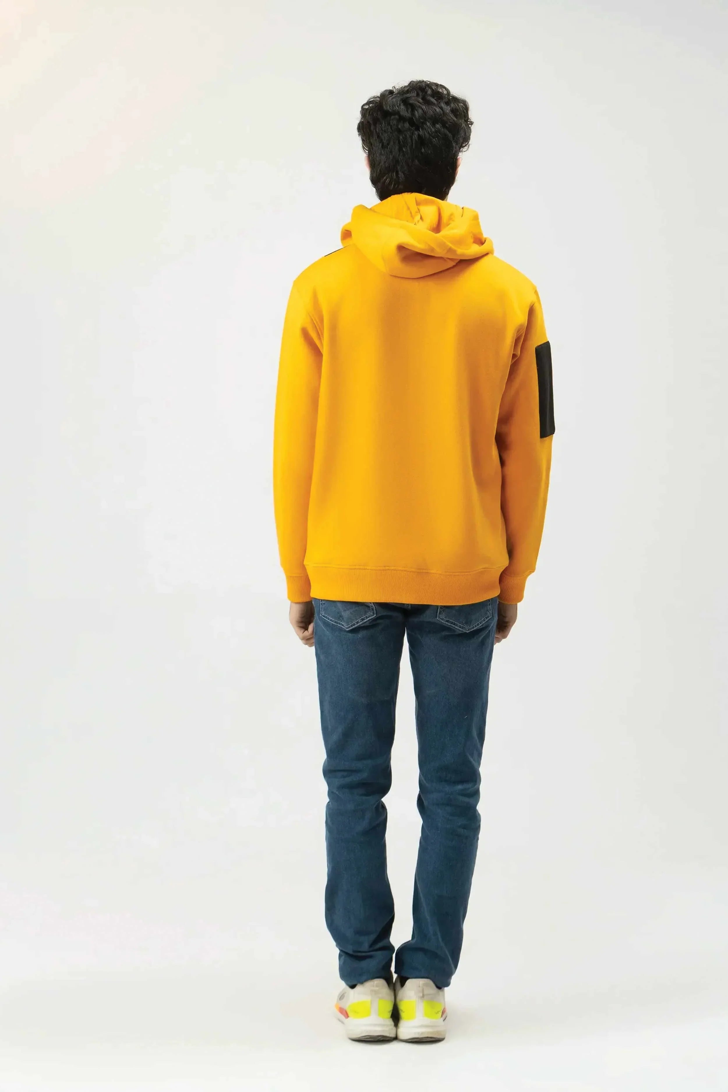 Person wearing a yellow hoodie and blue jeans on a white background