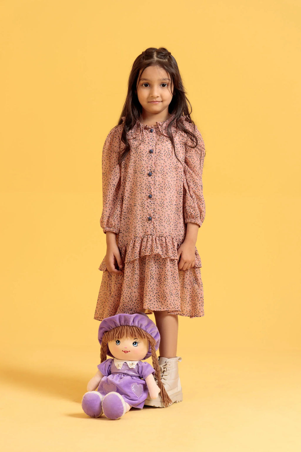 Young girl in a floral dress holding a purple doll against a yellow background