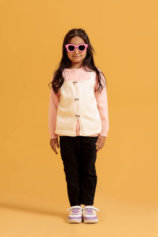 Young girl wearing a light pink jacket over a pink shirt, black pants, and purple shoes on an orange background